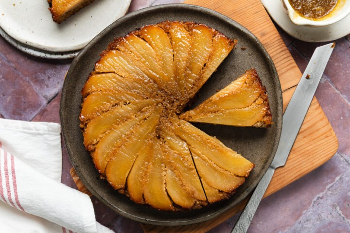 Homemade gluten-free pear upside down cake with three slices cut from it, one slice on a plate.