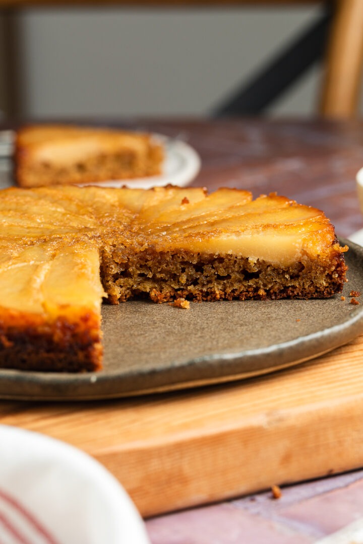 Side view of the pear cake with a slice cut out of it, to show the texture and layer of fresh pear on the top.