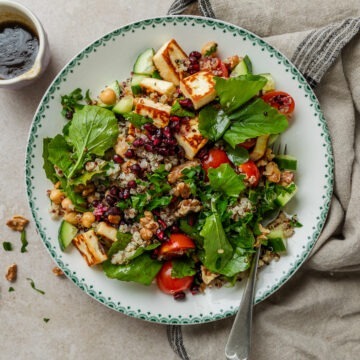 A bowl of halloumi and pomegranate salad with quinoa, with a spoon ready to serve.