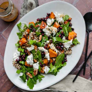 A serving platter of roasted pumpkin quinoa salad topped with goats cheese and pomegranate seeds.