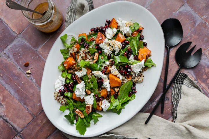A serving platter of roasted pumpkin quinoa salad topped with goats cheese and pomegranate seeds.