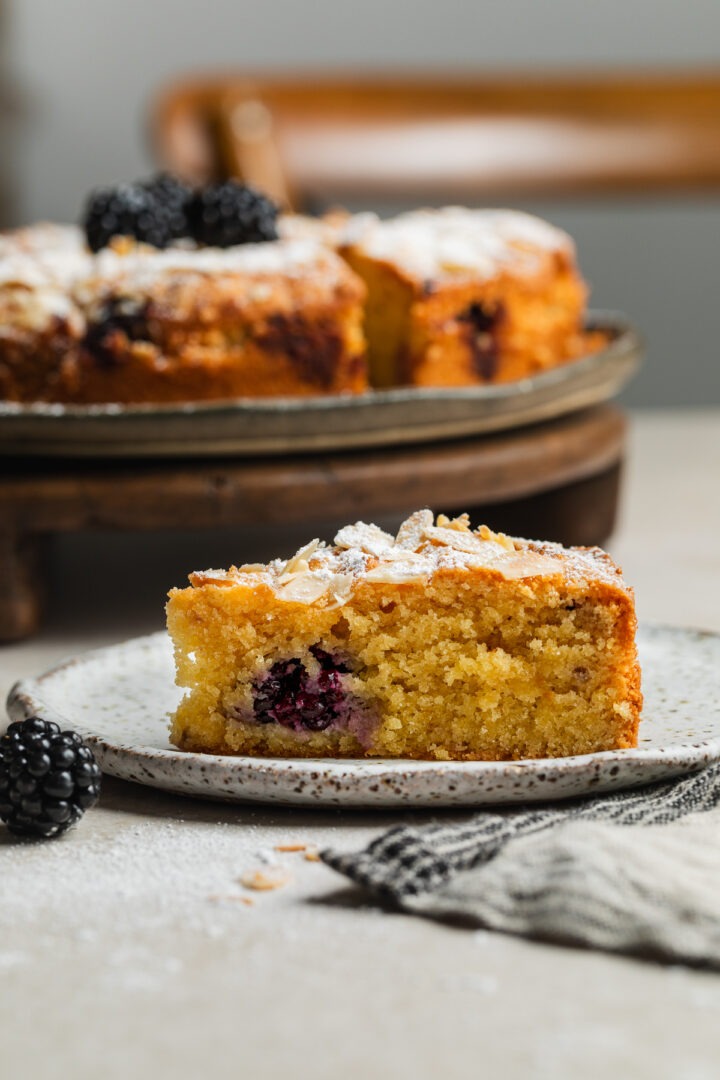 Side view of a slice of blackberry cake on a plate with the rest of the cake just visible behind.