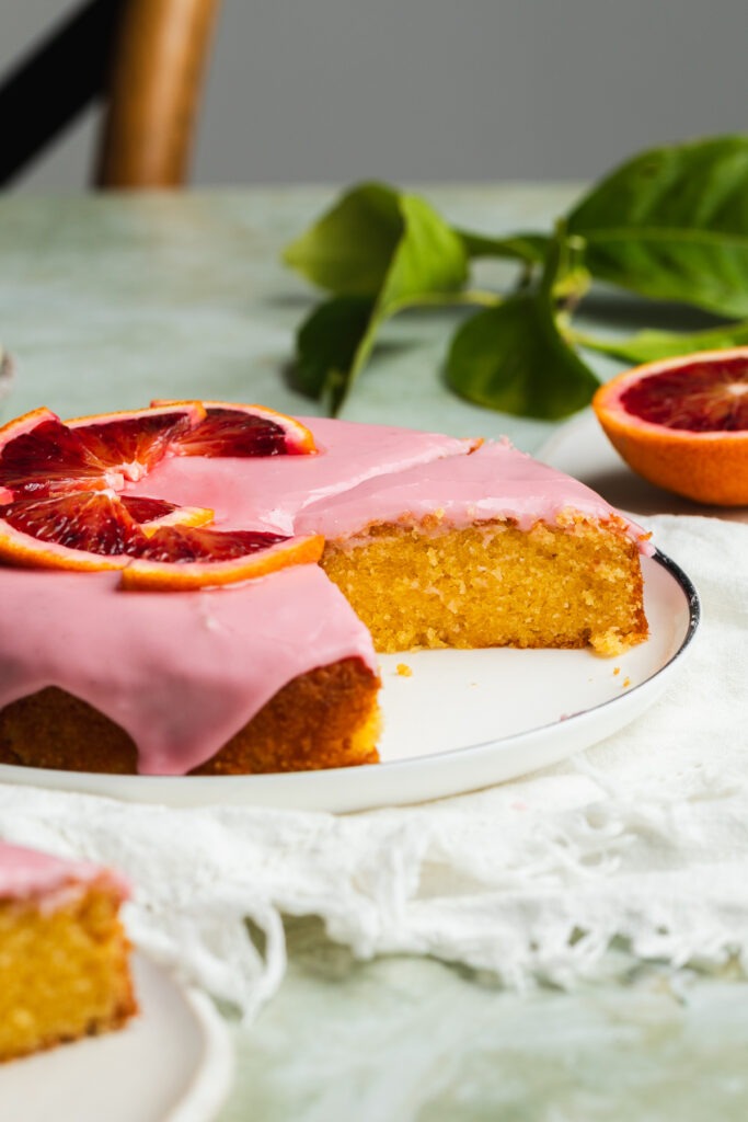 Blood orange almond cake served on a table with fresh blood oranges just visible in the background.