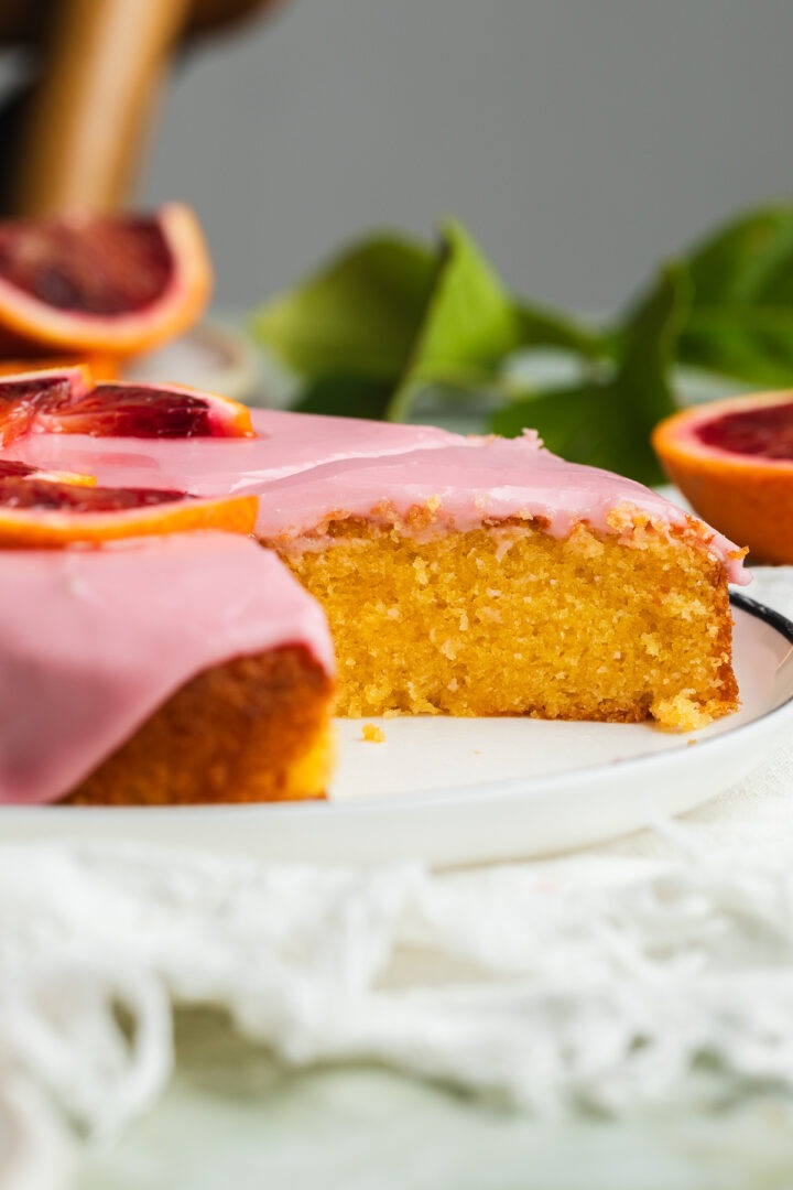 Side view of the cut homemade almond cake to show the almond sponge and pink blood icing topping.