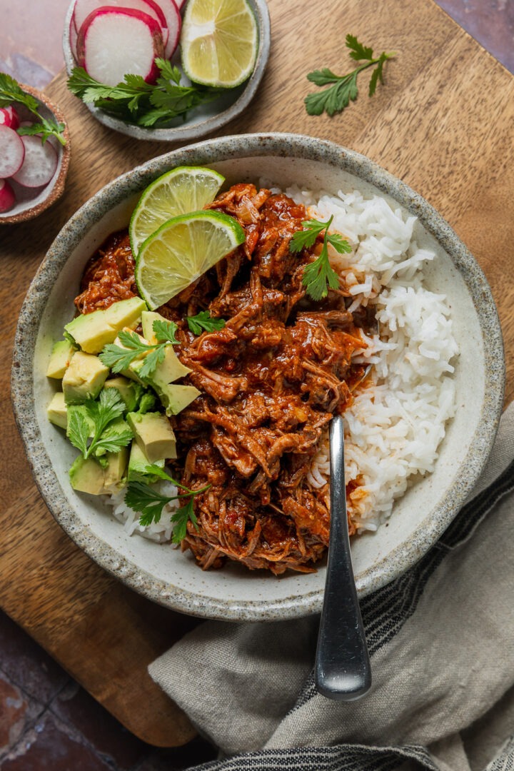 A bowl of homemade Mexican pulled beef served with rice, avocado and fresh lime.