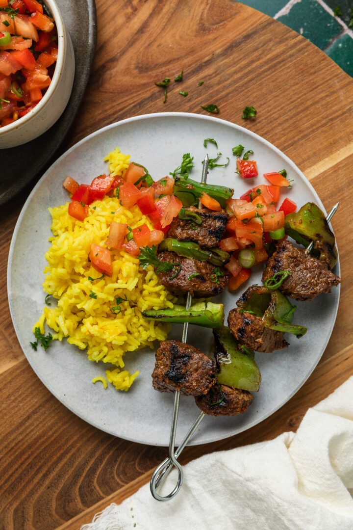 A plate of beef skewers served with turmeric rice and salsa.